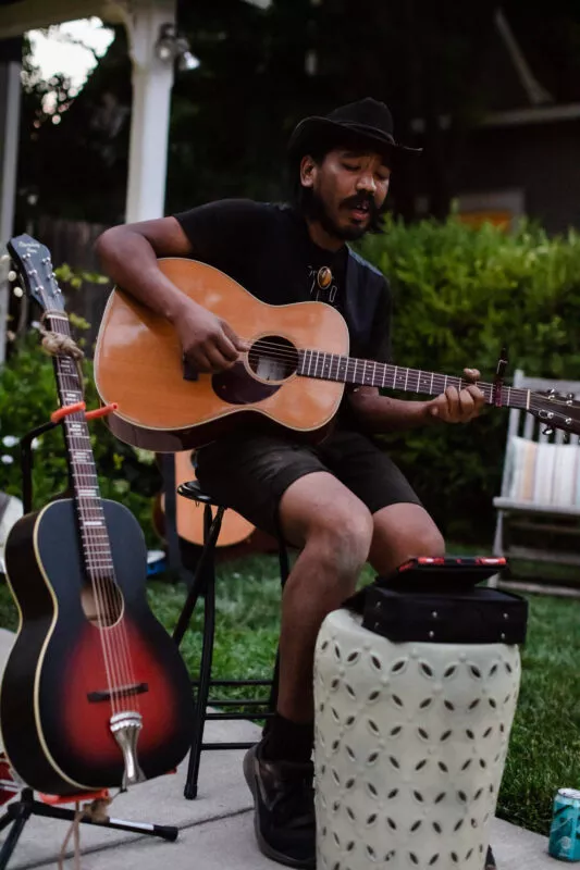 Guest performer playing guitar during a casual acoustic performance in the front yard of this Barber neighborhood home.