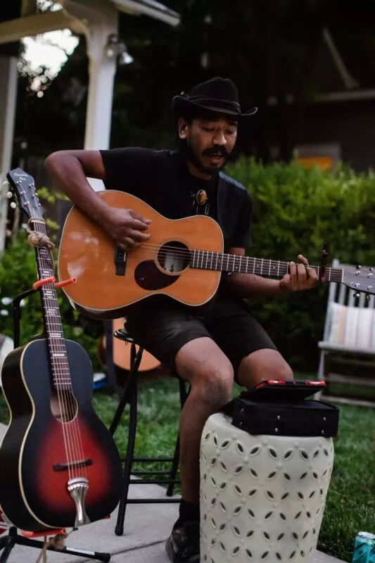 Guest performer playing guitar during a casual acoustic performance in the front yard of this Barber neighborhood home.