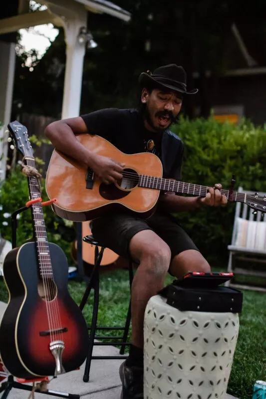 Guest performer playing guitar during a casual acoustic performance in the front yard of this Barber neighborhood home.